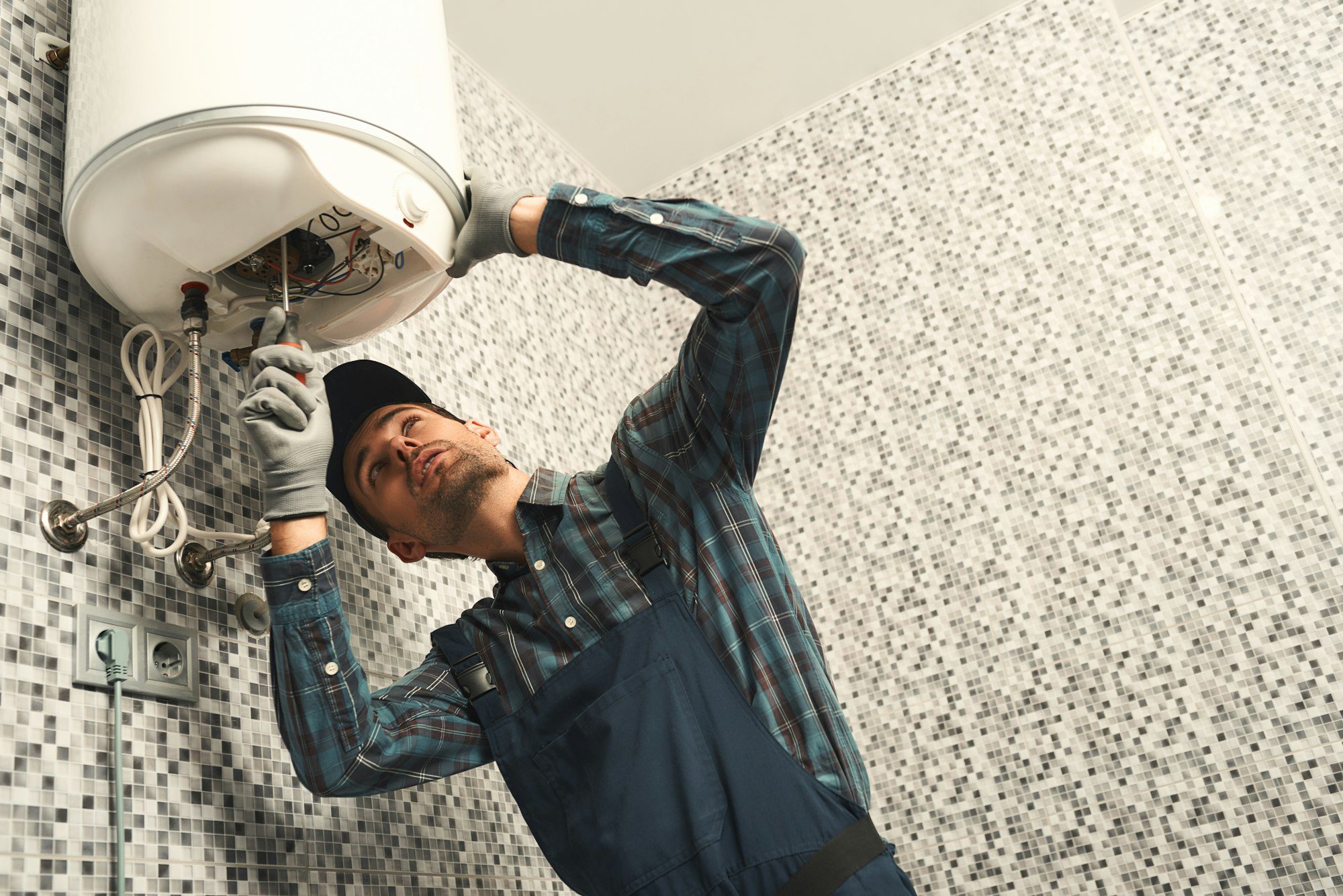 Plumber installing electric heating boiler. Young handyman in uniform setting up electric heating