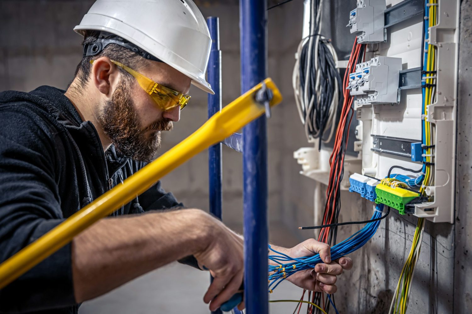 A male electrician works in a switchboard with an electrical connecting cable.