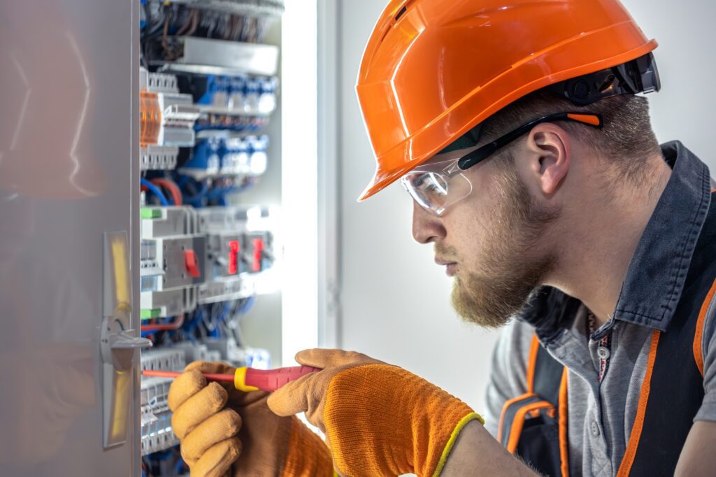 Male electrician working in switchboard. Male electrician in overalls working with electricity.